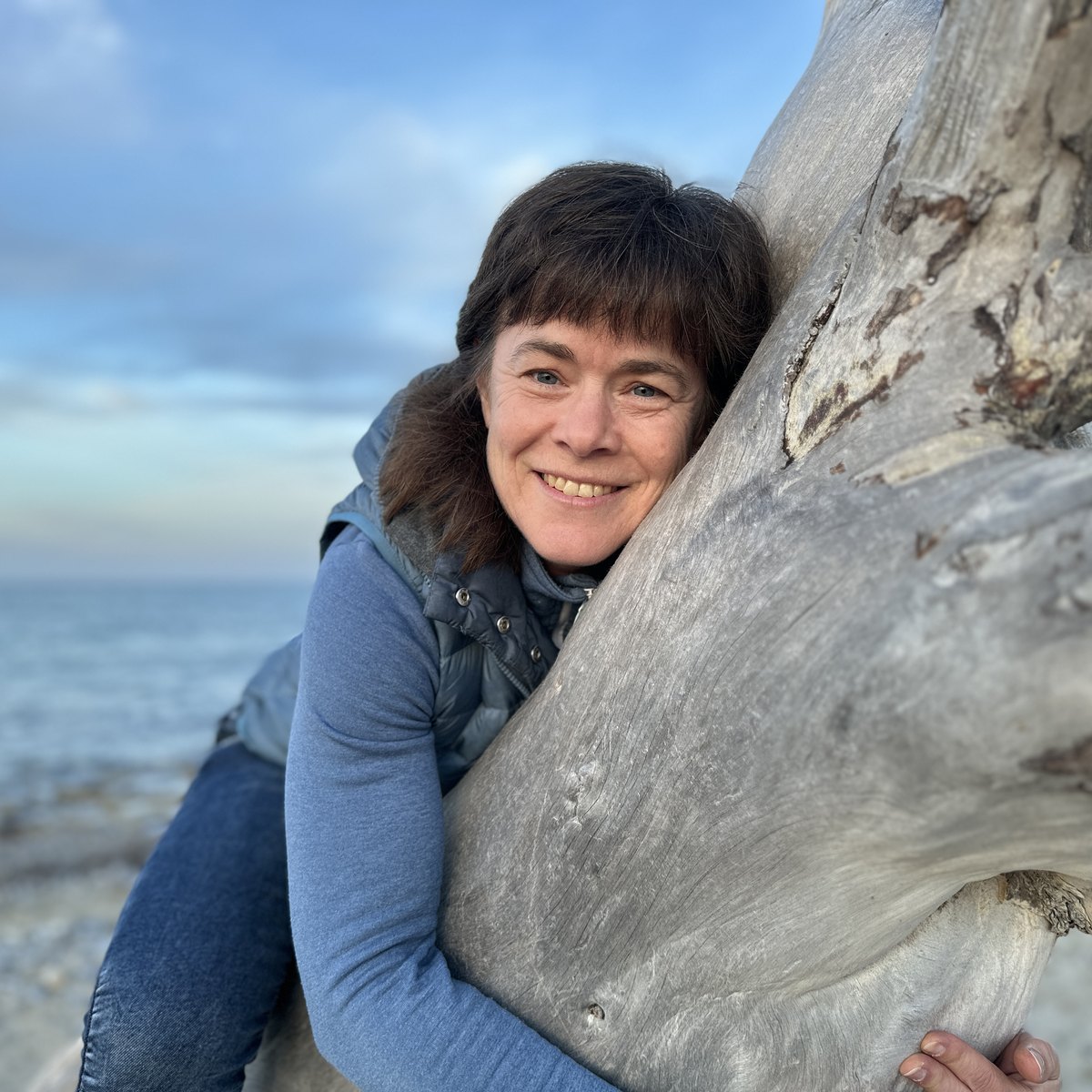 Sabine Giller am Strand, an einen Treibholzstamm gelehnt